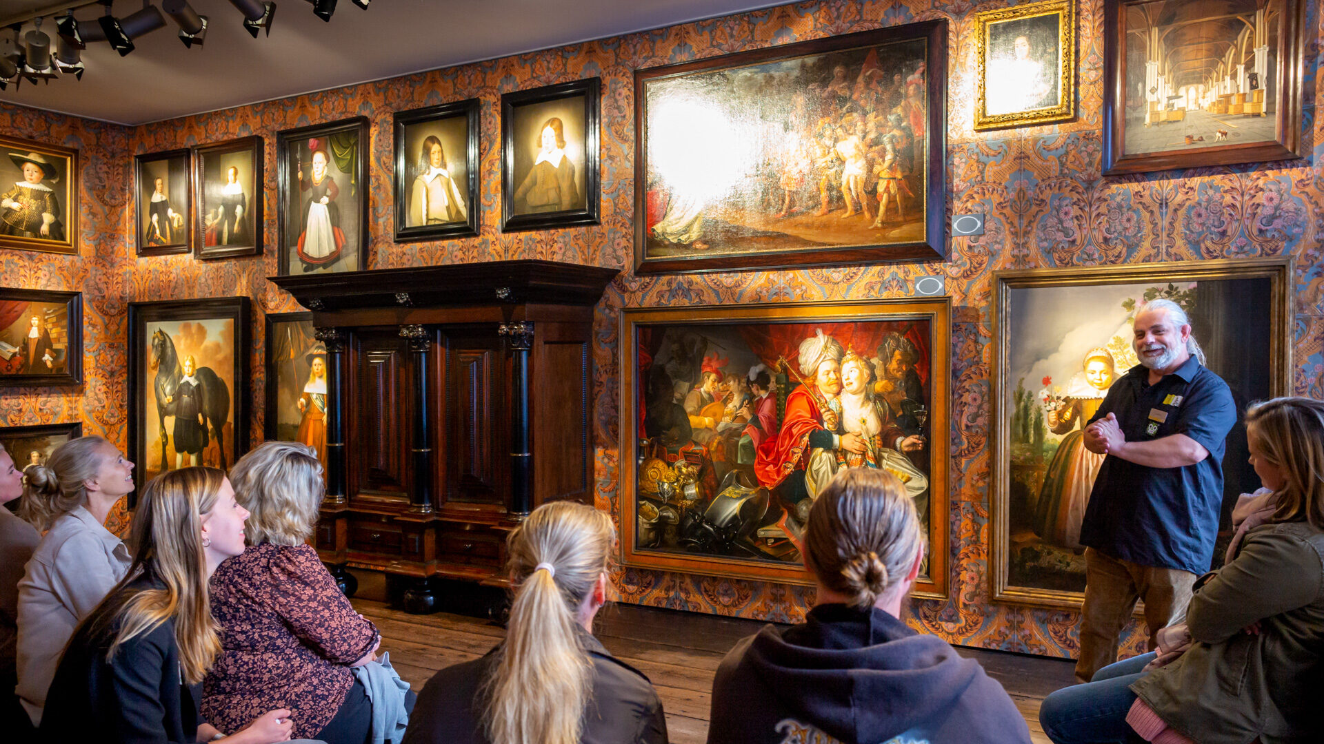 meerdere personen luisteren naar educator met schilderijen op achtergrond