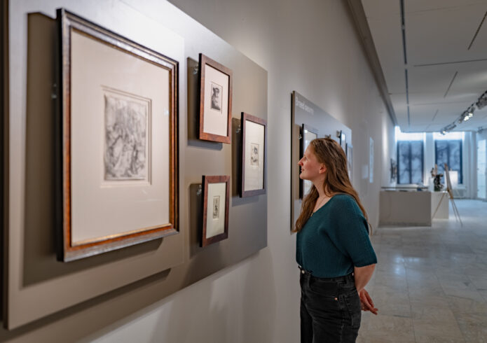 Witte ruimte met lichtgrijze panelen met etsen waar persoon naar kijkt