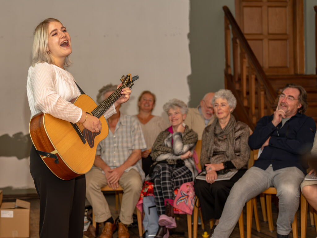 Persoon met gitaar die zingt voor groep mensen