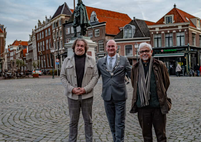 Drie personen kijkend naar camera voor standbeeld op plein met klinkers