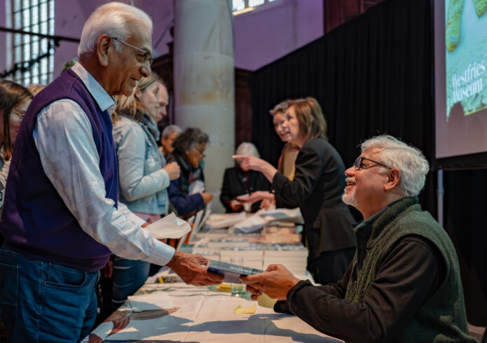 Zittend persoon geeft staand persoon een boek