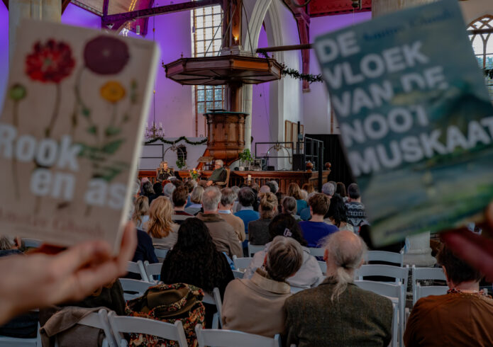 Twee boeken vaag op voorgrond en erachter een kerkzaal vol met mensen